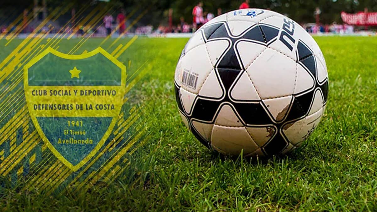 Pelota de fútbol en una cancha de césped con el escudo de Defensores de la Costa visible