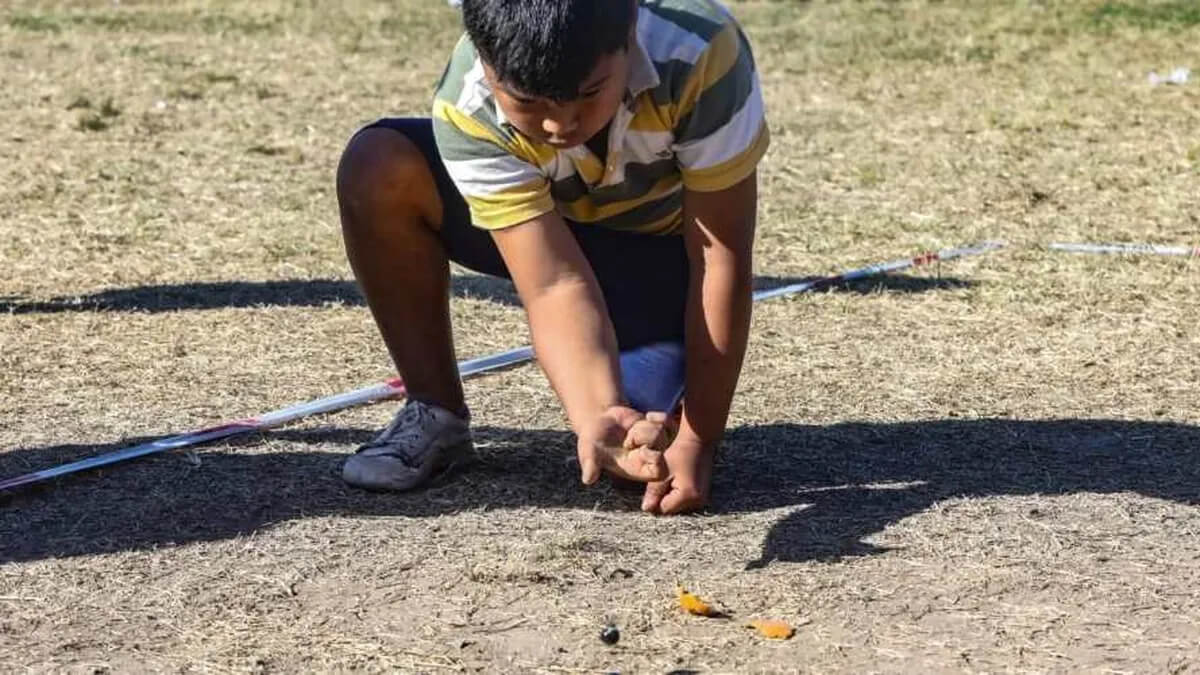 Niño jugando al tradicional juego de las bolitas en el suelo