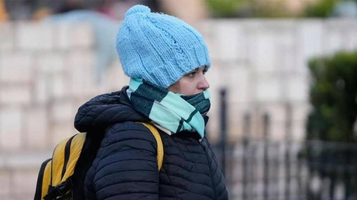 Mujer muy abrigada caminando en la vía pública ante ola de frío