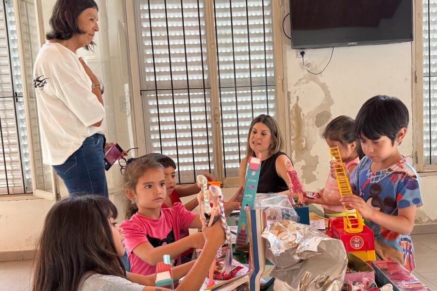 Charo Mancini dialogando con Laura Velozo mientras los niños de la Fundación San Miguel Arcángel abren los obsequios