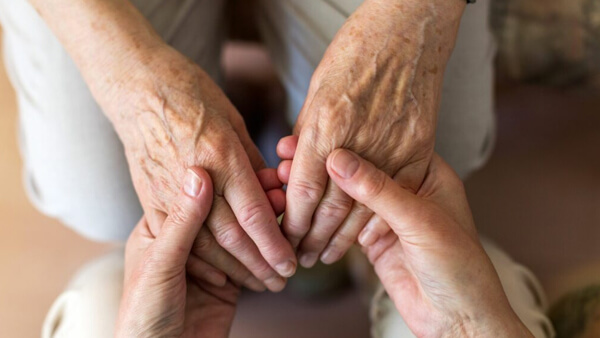 Manos de cuidador sosteniendo manos de persona mayor en señal de acompañamiento y cuidado