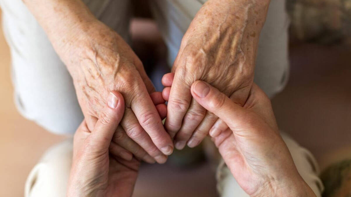 Manos de cuidador sosteniendo manos de persona mayor en señal de acompañamiento y cuidado